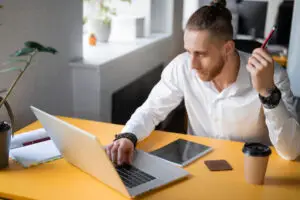 Consultant SEO en freelance assis à un bureau dans un environnement de bureau moderne, travaillant sur un ordinateur portable avec un carnet et un café à côté.